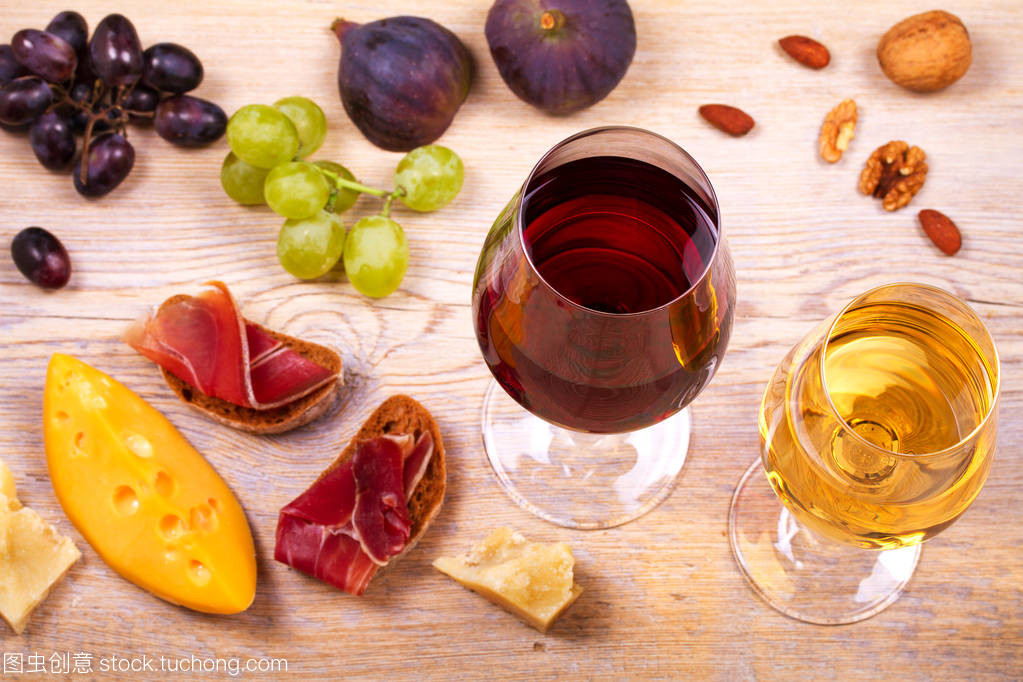 紅色和白色奶酪、 火腿、 無花果和葡萄與葡萄酒杯。木制的桌子上的酒杯。葡萄酒的靜物